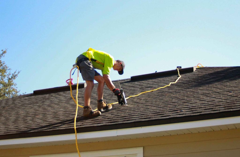 Roofer with safety harness installing shingles on a sunny Southern California home
